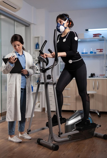 Mujer corredora atleta que usa electrodos médicos que trabajan en la resistencia corporal haciendo ejercicio cardiovascular en el laboratorio mientras la investigadora científica monitorea la frecuencia cardíaca. Médico médico examinando datos de electrocardiograma
