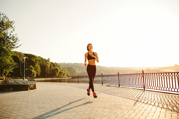 Mujer corriendo Corredor trotar en la luz del sol brillante. Modelo femenino de entrenamiento físico fuera en el parque