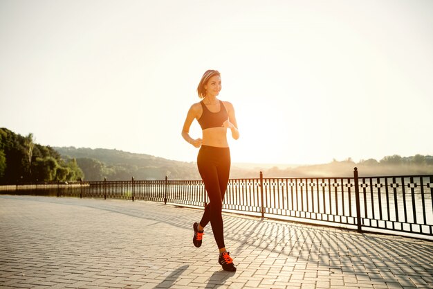 Mujer corriendo Corredor trotar en la luz del sol brillante. Modelo femenino de entrenamiento físico fuera en el parque