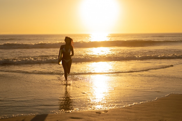 Mujer corriendo con tabla de surf en la playa