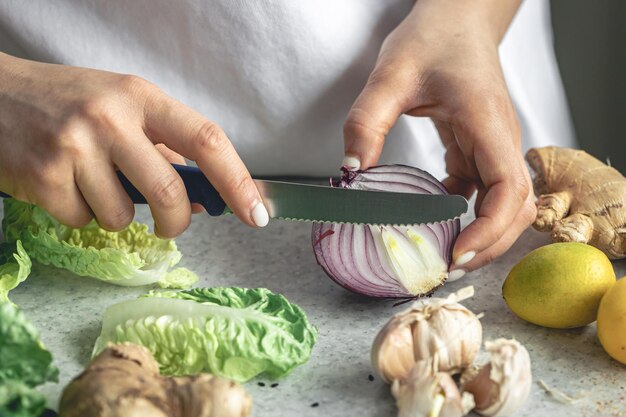 Una mujer corta cebollas para ensalada en el primer plano de la mesa de la cocina