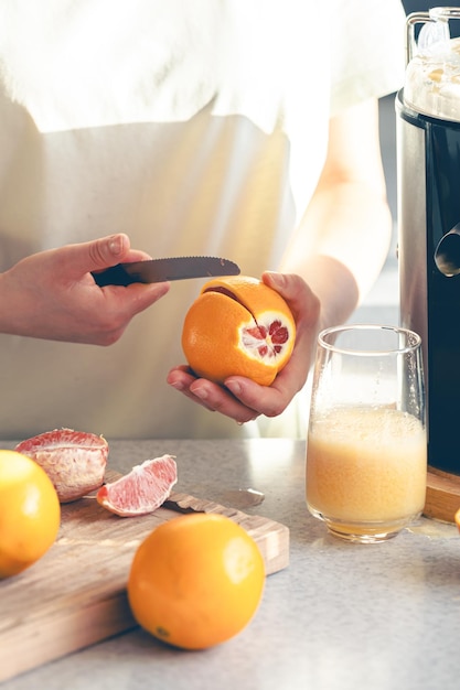 Foto gratuita una mujer corta una naranja en la cocina y hace jugo en un exprimidor