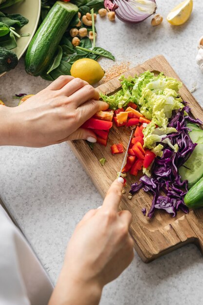 Foto gratuita una mujer corta un pimienta fresca en una tabla de madera en la cocina