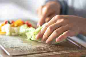 Foto gratuita una mujer corta verduras en una tabla de cortar
