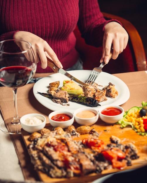 mujer cortando filete de pollo a la parrilla servido con pimientos asados, ensalada y vino