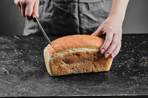 Mujer cortando pan con cuchillo en el escritorio oscuro.