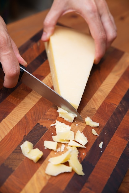 Mujer cortando parmesano en tablero de madera