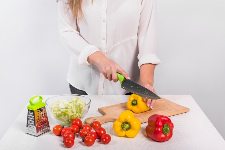 Foto gratuito mujer cortando pimiento amarillo sobre tabla de madera
