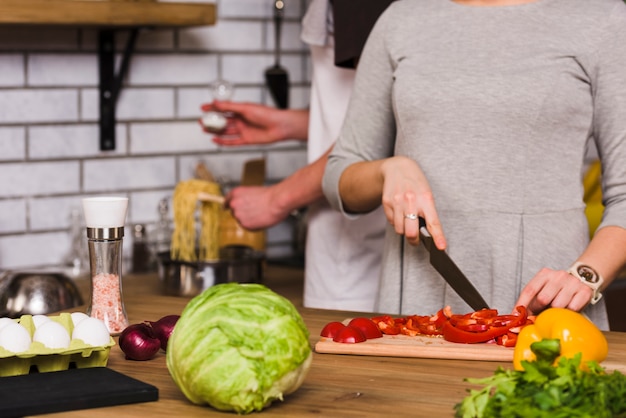 Mujer cortando pimiento rojo y pasta salada hombre