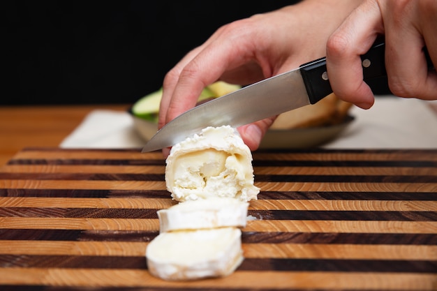 Mujer cortando queso blando en tablero de madera