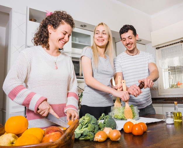 Mujer cortando verduras y joven pareja preparando ensalada en la cocina