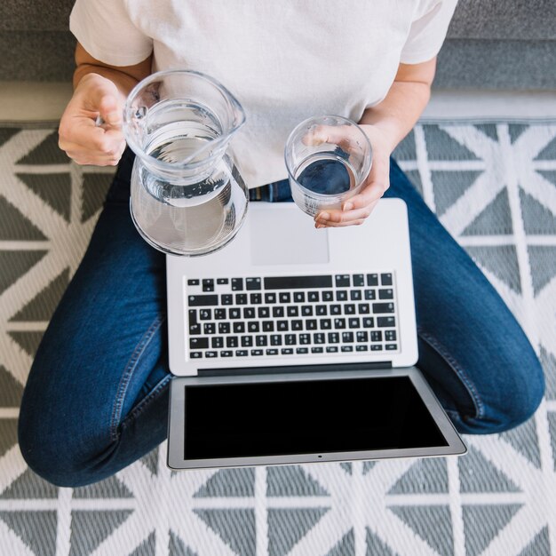 Mujer de la cosecha con agua que vierte de la computadora portátil