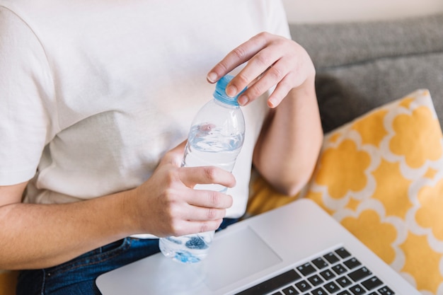 Mujer de la cosecha con la botella de agua de la abertura de la computadora portátil