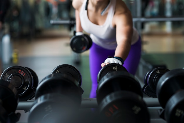 Mujer de la cosecha que levanta pesa de gimnasia en gimnasio