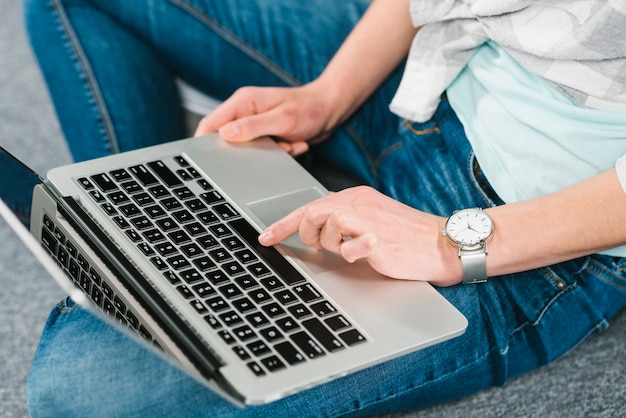 Mujer de la cosecha que usa la computadora portátil moderna en piso