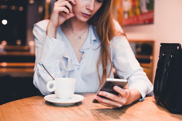 Mujer de la cosecha que usa smartphone en la tabla del café