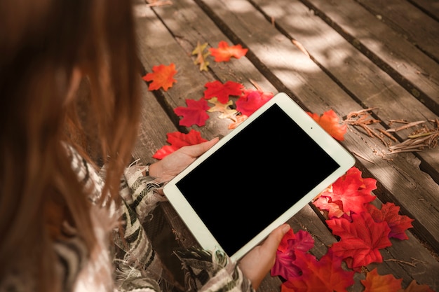 Mujer de la cosecha que usa la tableta en parque del otoño