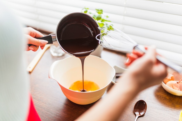 Mujer de la cosecha que vierte la salsa de chocolate en los huevos