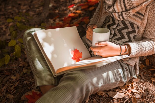 Mujer de la cosecha con taza de lectura en el bosque de otoño