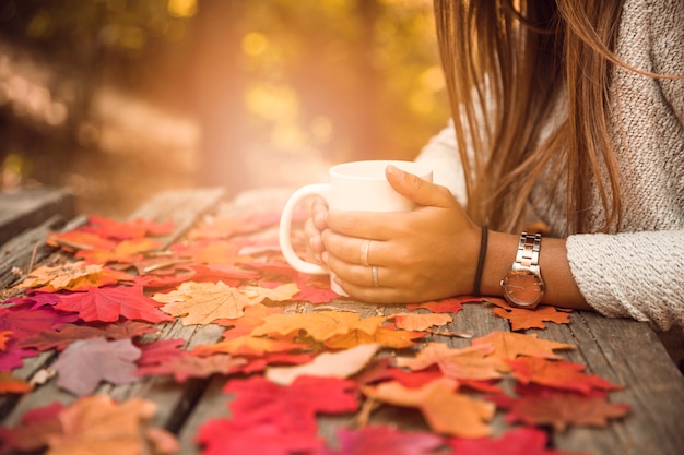 Mujer de la cosecha con la taza en la mesa en el parque de otoño