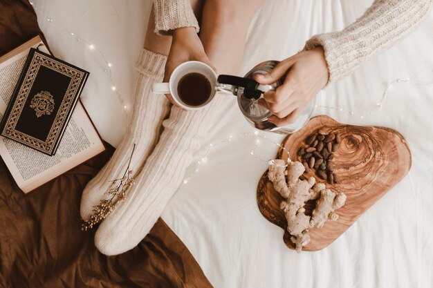 Mujer de cosecha verter bebida cerca de libros y aperitivos