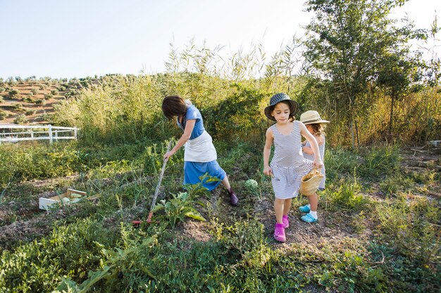 Mujer cosechando vegetales en campo con sus hijas