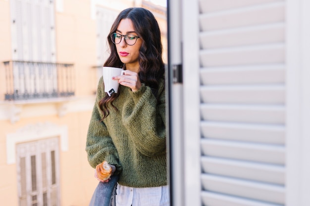 Mujer con croissant soplando en la bebida caliente