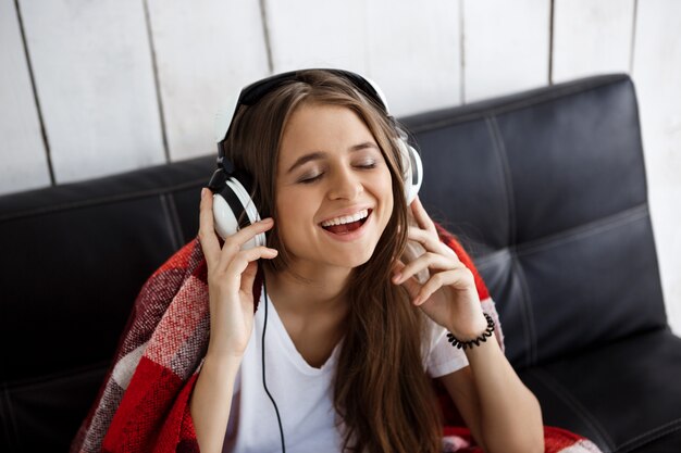 Mujer en cuadros escuchando música en auriculares, sentado en el sofá.