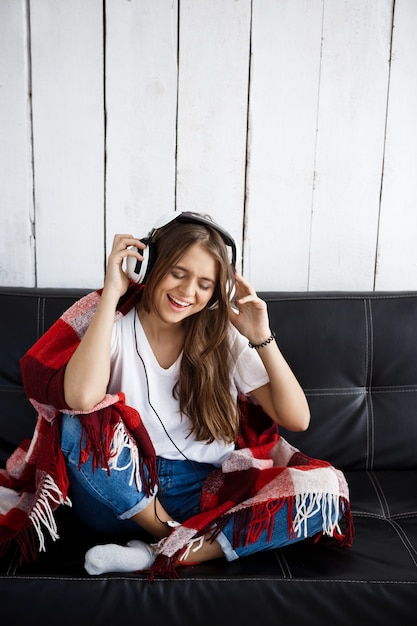 Mujer en cuadros escuchando música en auriculares, sentado en el sofá.