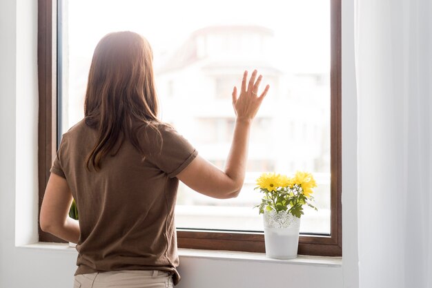 Mujer en cuarentena en casa mirando por la ventana