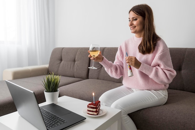 Foto gratuita mujer en cuarentena celebrando un cumpleaños con amigos a través de una computadora portátil y una bebida