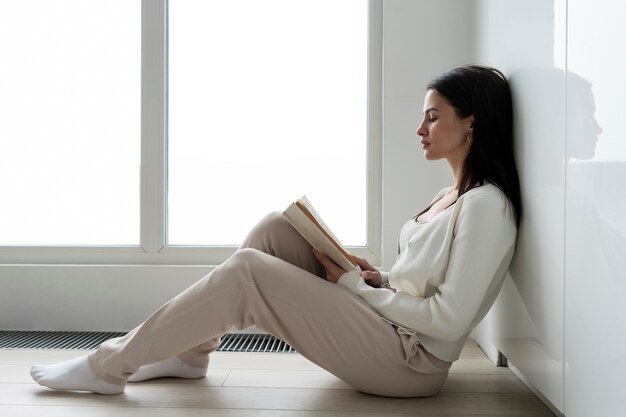 Mujer en cuarentena de tiro completo leyendo en el piso