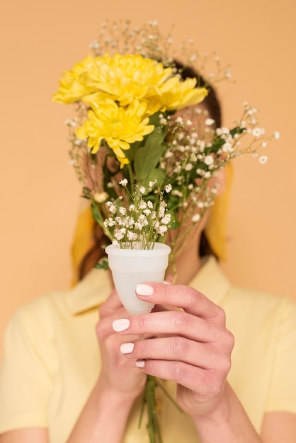 Mujer cubriendo el rostro con flores en vaso de plástico