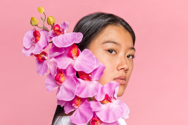 Mujer cubriéndose la cara con orquídeas y mirando a cámara