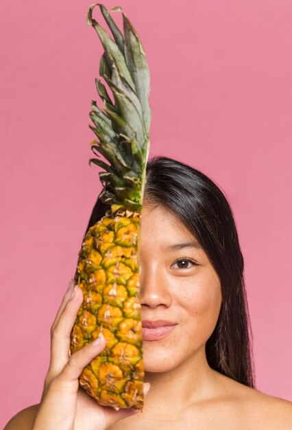 Mujer cubriéndose la cara con piña y mirando a cámara