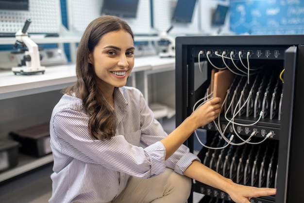 Mujer en cuclillas cerca de equipos especiales sonriendo a la cámara