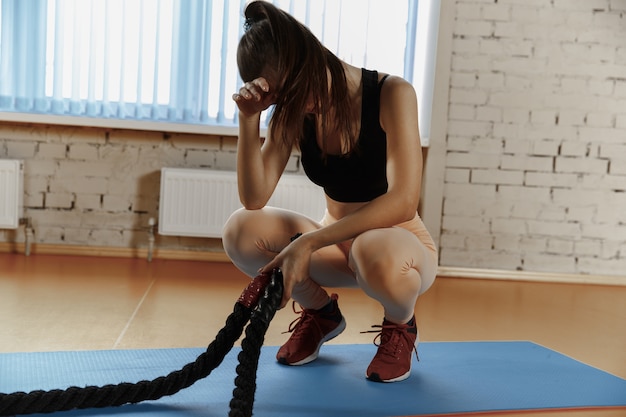Mujer con cuerdas de batalla ejercicio en el gimnasio. Atleta, deporte, cuerda, entrenamiento, entrenamiento, ejercicios y concepto de estilo de vida saludable