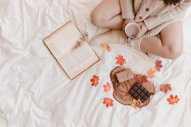 Mujer de cultivo con café y libro cerca de chocolate y regalo