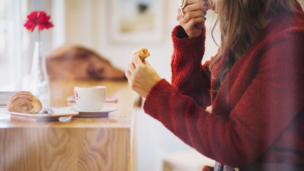 Mujer de cultivo comiendo croissant en café