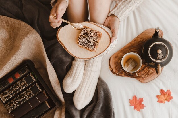 Mujer de cultivo comiendo panal cerca de libros y té