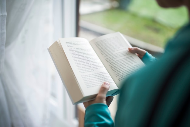 Mujer de cultivo disfrutando de libro junto a la ventana