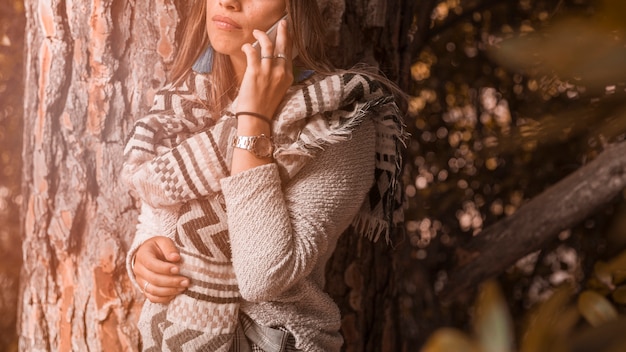 Mujer de cultivo hablando en el teléfono inteligente cerca de un árbol