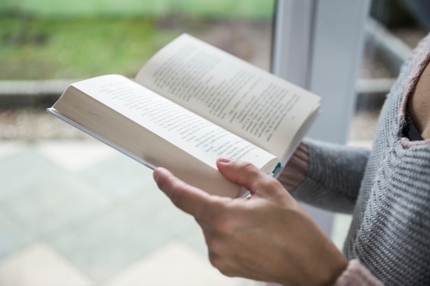 Mujer de cultivo leyendo cerca de la ventana