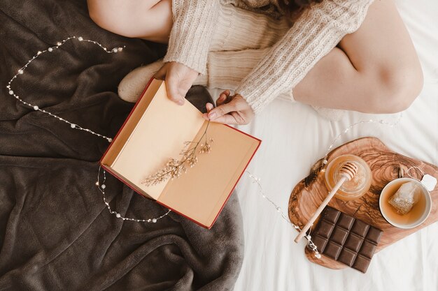 Mujer de cultivo con libro cerca de té y dulces