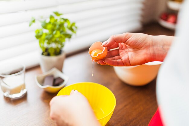 Mujer de cultivo poniendo huevos crudos en un tazón