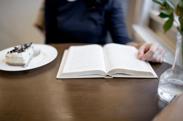 Mujer de cultivos disfrutando de postre y libro de lectura