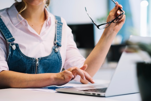 Foto gratuita mujer de cultivos con gafas trabajando en la computadora portátil