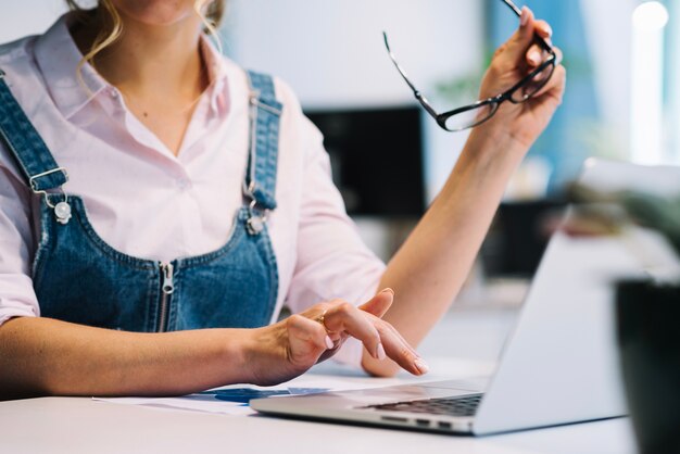 Mujer de cultivos con gafas trabajando en la computadora portátil