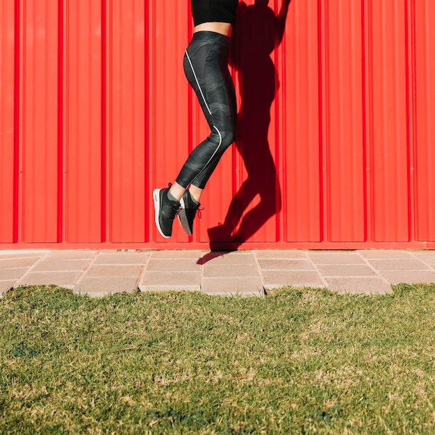 Mujer de cultivos saltando cerca de la pared roja