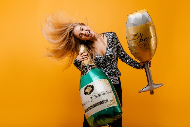 Mujer de cumpleaños emocionada bailando con botella de champán. Retrato de mujer emotiinal positiva jugando después de la fiesta.